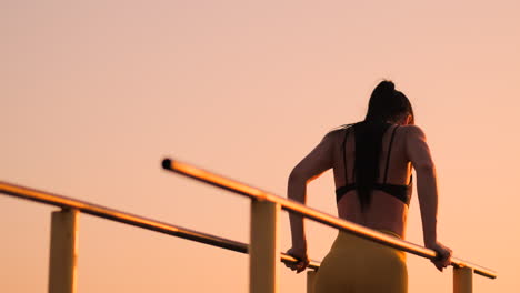 Slow-motion:-a-Beautiful-woman-athlete-doing-push-UPS-on-bars-in-a-black-tank-top-in-great-shape-and-yellow-pants-with-dark-hair.